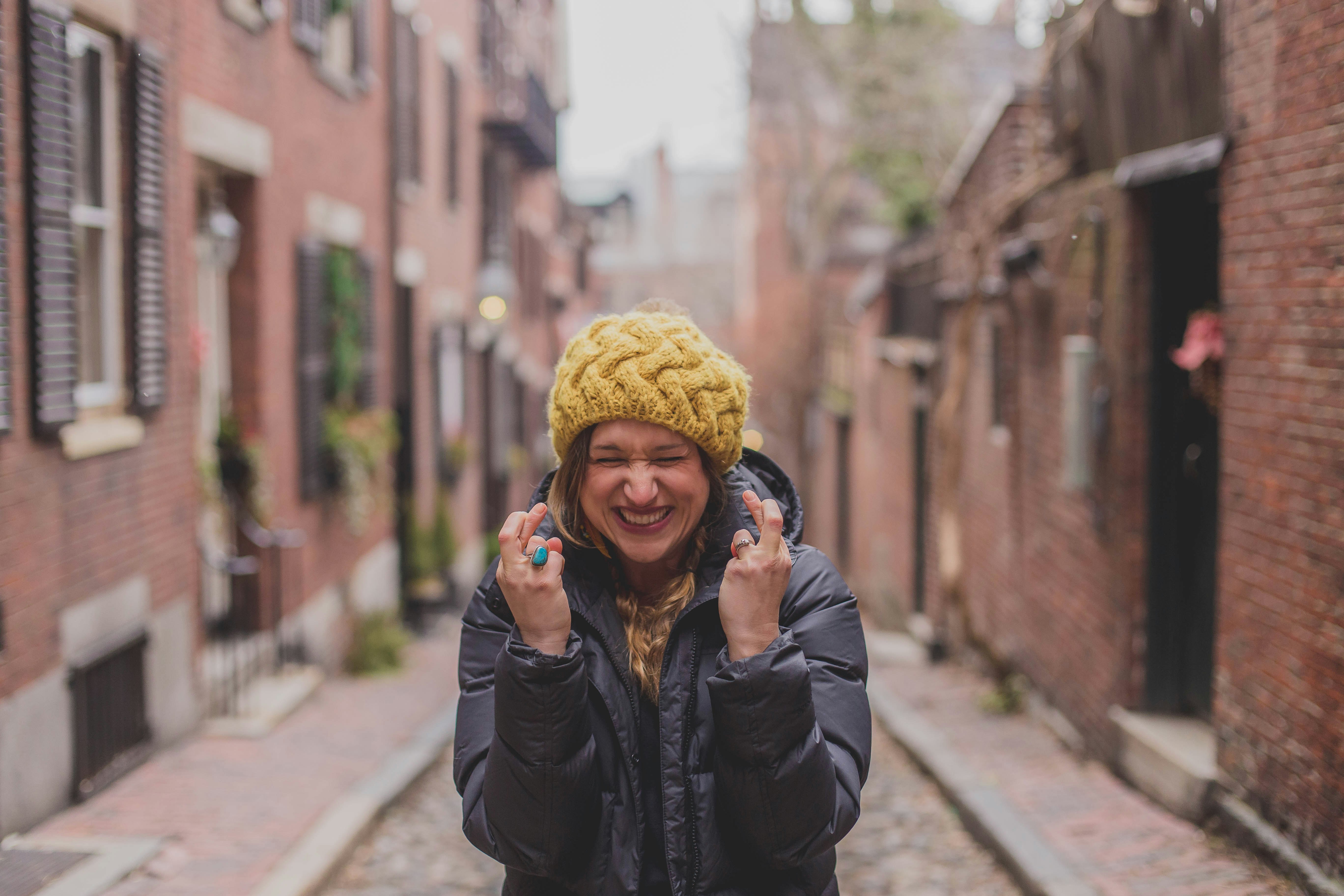 woman in black jacket and yellow knit cap standing on sidewalk during daytime